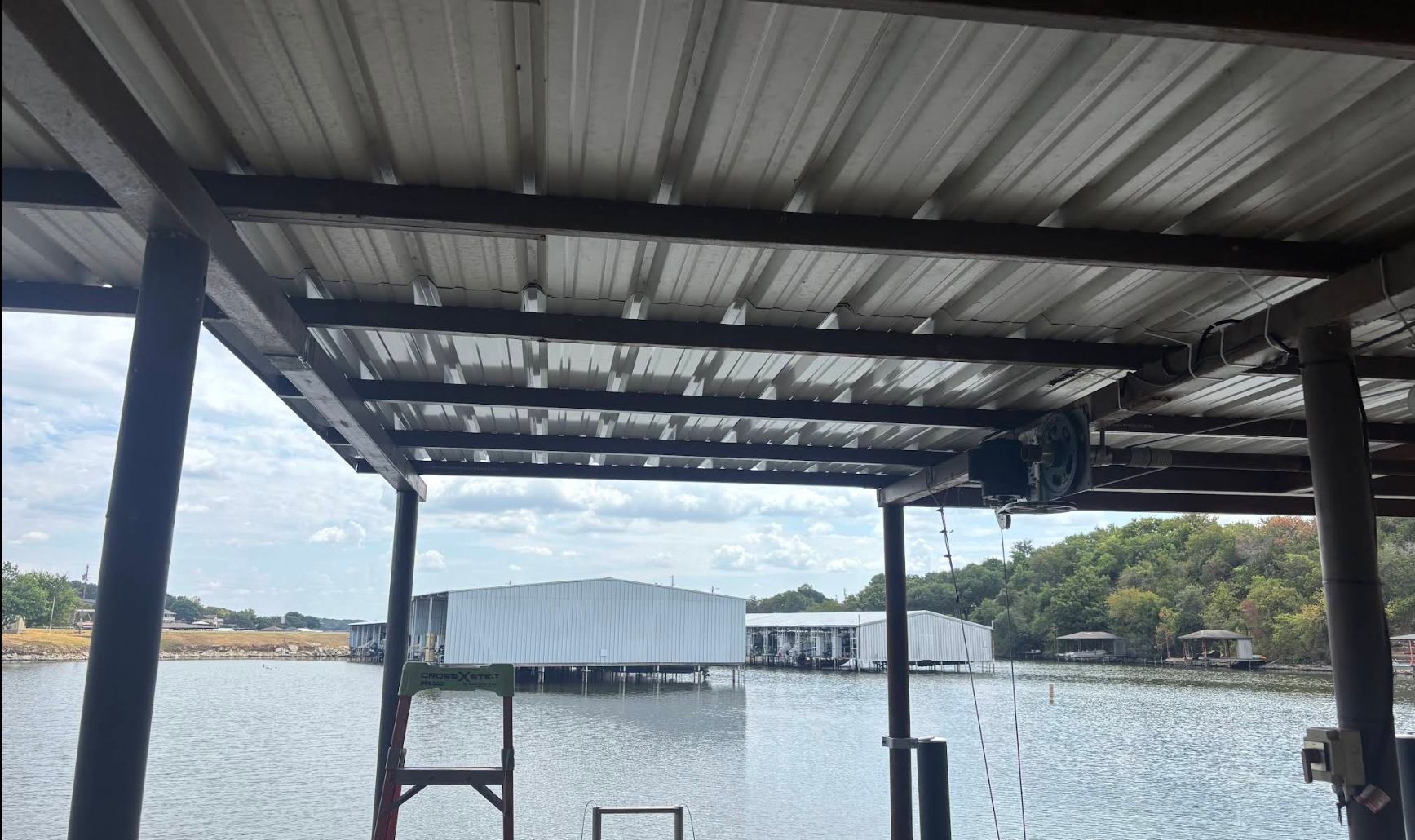 Steel-framed covered boat slip with a metal roof and a boat lift winch over open lake water